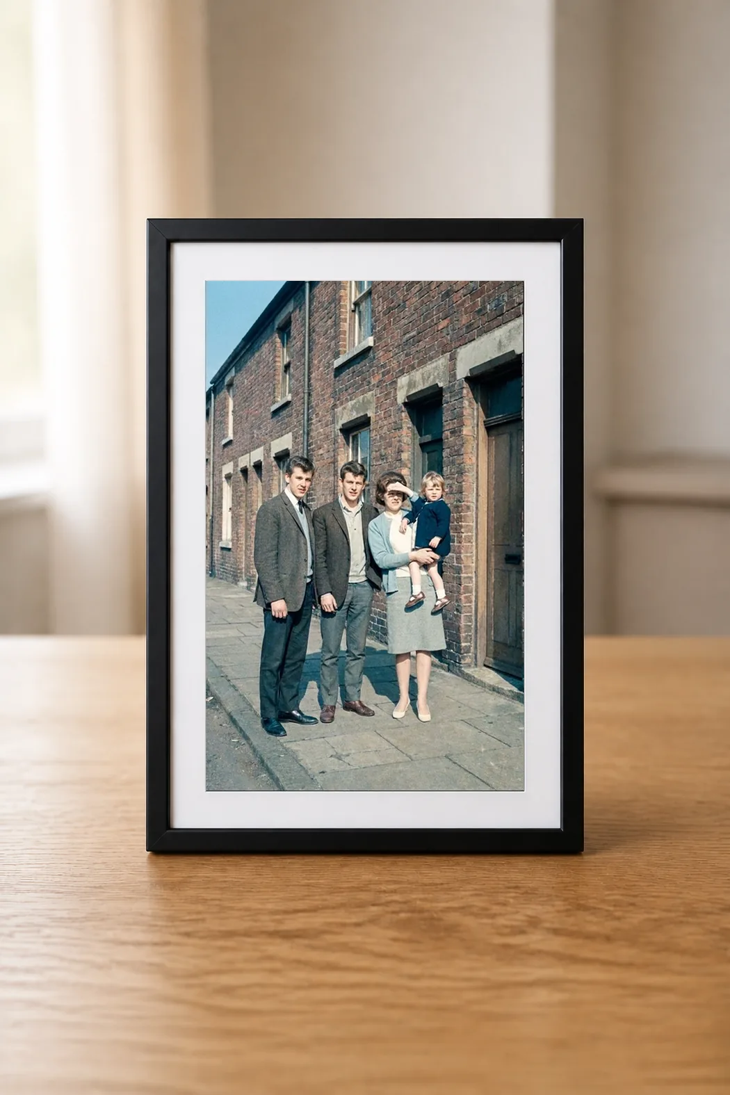 De digitale fotolijst op een eiken tafel, met een herstelde familiefoto uit de jaren zestig op het scherm.